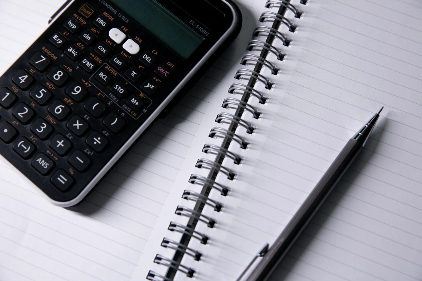 Calculator, open notebook and pen on a desk