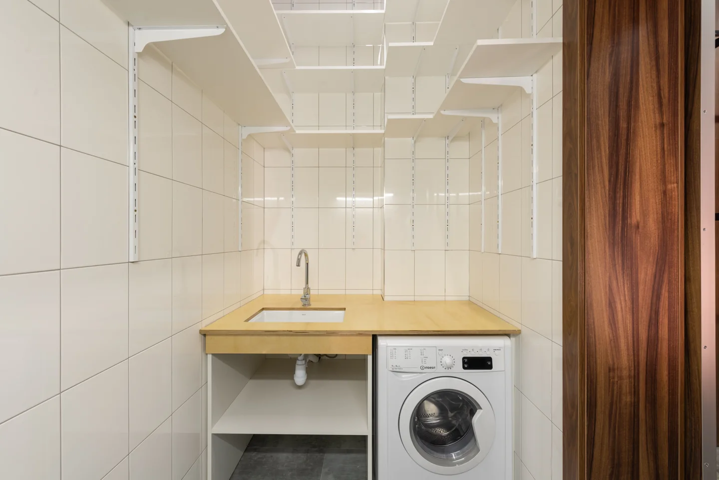 A white washing machine beneath a wooden worktop in a tiled utility room