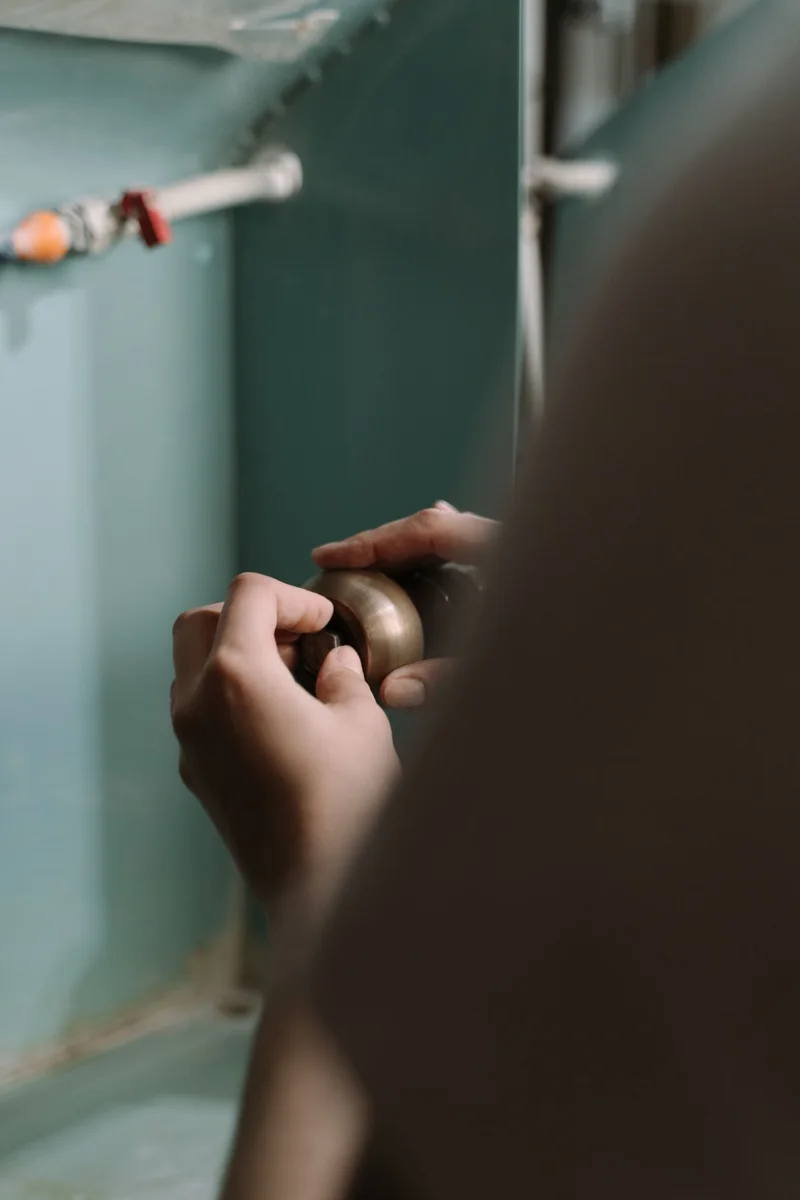 Hands working on plumbing beneath a kitchen sink.
