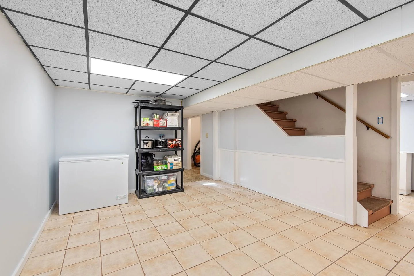 Basement interior with tiled floor, shelving, and a staircase.