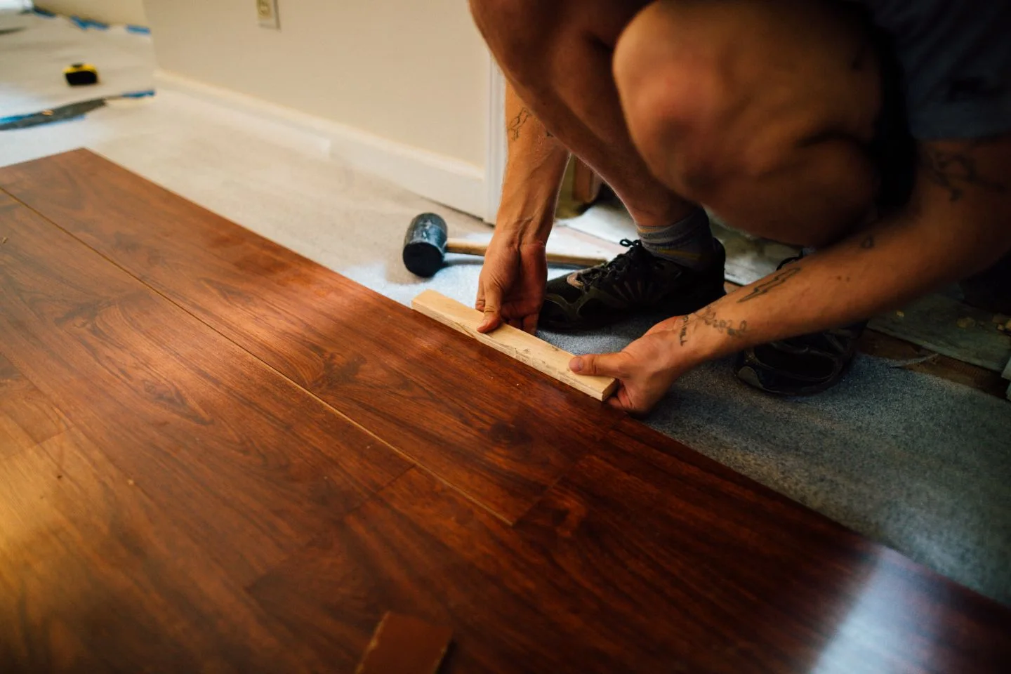 A person fitting laminate floorboards indoors.