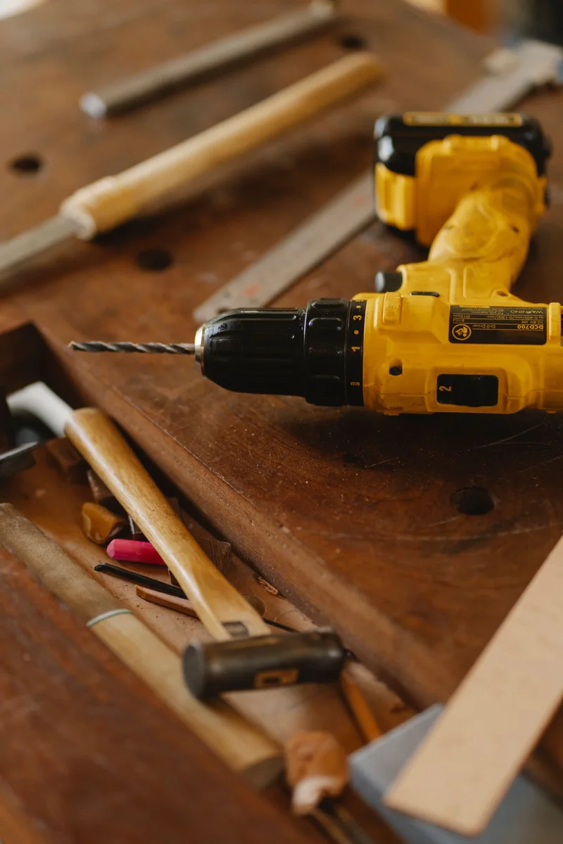 A yellow electric drill lies among hand tools on a wooden workbench