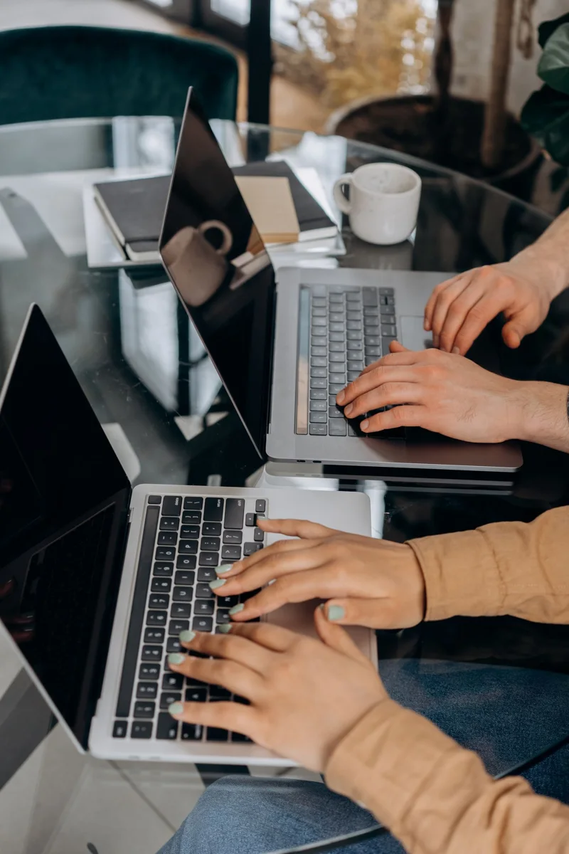Two people use laptops at a glass table